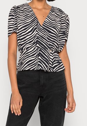 Kvinde iført en sort-hvid zebra-stribet V-hals bluse med korte puffede ærmer og sorte bukser med høj talje.