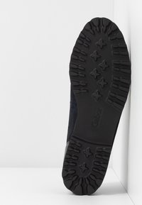 Podeszwa czarnego buta z głębokimi rowkami i wzorami w kształcie krzyża, z marką "Gabor", ustawiona pod kątem na białym tle.