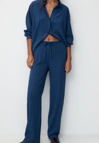 Marinblå pyjamas set som innehåller en skjorta med knappar och rullade ärmar samt byxor med avslappnad passform, elastisk midja och dragsko. Vertikala ränder.