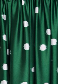 Tissu vert avec des plis froncés présentant des cercles blancs dispersés aux bords légèrement flous.