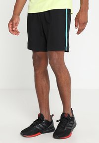 Pantalones cortos deportivos negros con una franja lateral turquesa, fabricados en material ligero. Llevados con zapatillas negras con acentos rojos.