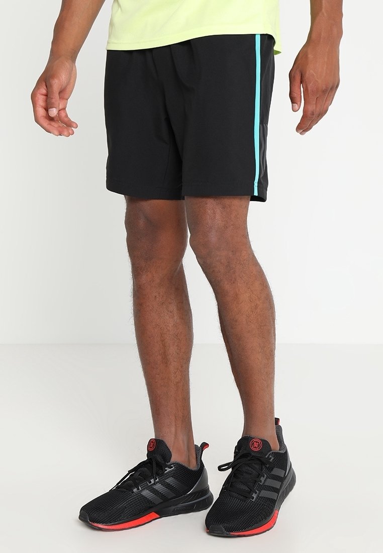 Pantalones cortos deportivos negros con una franja lateral turquesa, fabricados en material ligero. Llevados con zapatillas negras con acentos rojos.