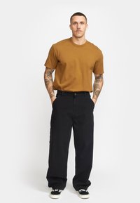 Camiseta marrón de manga corta combinada con pantalones anchos negros y zapatillas negras. Los pantalones tienen un cierre de botón y bolsillos laterales.