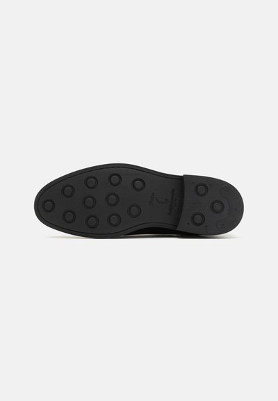 Black rubber shoe sole with circular grip patterns, smooth texture, slight arch, and rounded toe. Features branding on the side.