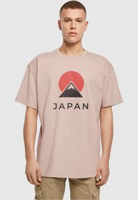 Camiseta de algodón rosa claro con un dise�ño gráfico de un sol rojo y la silueta de una montaña, con el texto "JAPÓN" en letras negras en negrita.