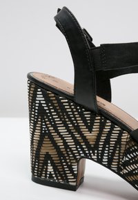 Sandale à talons hauts en cuir noir avec une plateforme en tissage noir, beige et blanc, dotée d'une bride pour la cheville et d'une semelle intérieure rembourrée.