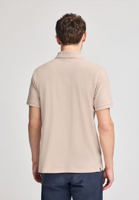 Camiseta polo beige con un cuello clásico y mangas cortas, hecha de una tela suave. Cuenta con un corte recto y un diseño mínimo.