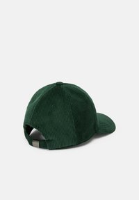 Gorra de pana verde con visera curva, tejido texturizado y una correa ajustable en la parte posterior. Presenta detalles bordados y agujeros de ventilación.