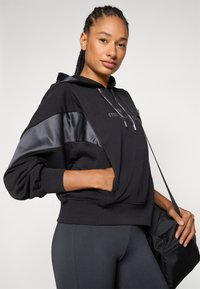 Svart hettegenser med satin detaljer, snorhett og frontlomme. Brukt sammen med svarte leggings og en svart veske. Glatt tekstur og avslappet passform.