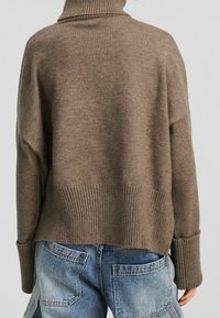 Brązowy, gruby sweter z dzianiny z wysokim prążkowanym kołnierzem i oversize'owym krojem. Posiada szerokie prążkowane mankiety oraz dół z teksturowanym wykończeniem.