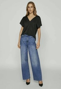 Čierny, krátky rukáv top s výstrihom do V, kombinovaný so svetlomodrými, širokými džínsami. Model má na sebe čierne vysoké podpätky. Hladké textúry a voľný strih.