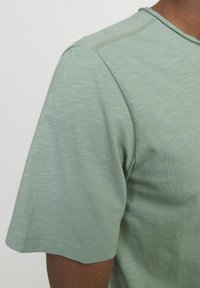 Short-sleeved green t-shirt with a textured, heathered finish, featuring a round neck and visible stitching details on the shoulder.
