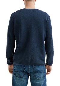 Marineblauwe gebreide trui met lange mouwen en een gestructureerd patroon, getoond vanaf de achterkant, in combinatie met denim jeans.