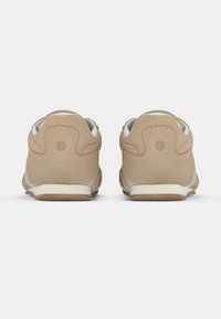 Αθλητικά παπούτσια σε καφέ χρώμα με λείο πάνω μέρος, λευκές λεπτομέρειες και επενδυμένη σόλα, με στρογγυλεμένη φτέρνα και υφή πίσω πάνελ.