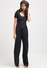 Svart bodysuit med korta ärmar, som kombineras med löst sittande svarta loungebyxor med justerbart snöre i midjan. Slät textur.