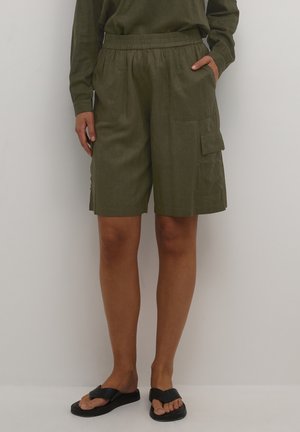 Personne portant un short cargo vert olive arrivant aux genoux avec une taille élastique, associé à des sandales noires à enfiler.