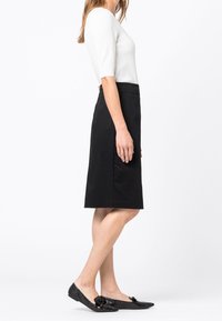 Černá šedá sukně ke kolenům vyrobená z hladké tkaniny, doplněná o přiléhavý bílý top. Obuv zahrnuje černé texturované baleríny s mašlí.