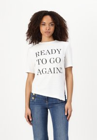 Balta medvilnės marškinėliai su užrašu "READY TO GO AGAIN!" ryškiu juodu šriftu. Trumpomis rankovėmis, laisvu siluetu ir šiek tiek asimetriniu apvadu.