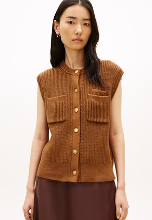 Barna kötött ujjatlan kardigán bordázott textúrával, arany gombokkal és két első zsebbel. Lekerekített nyakkivágás és testhezálló szabás.