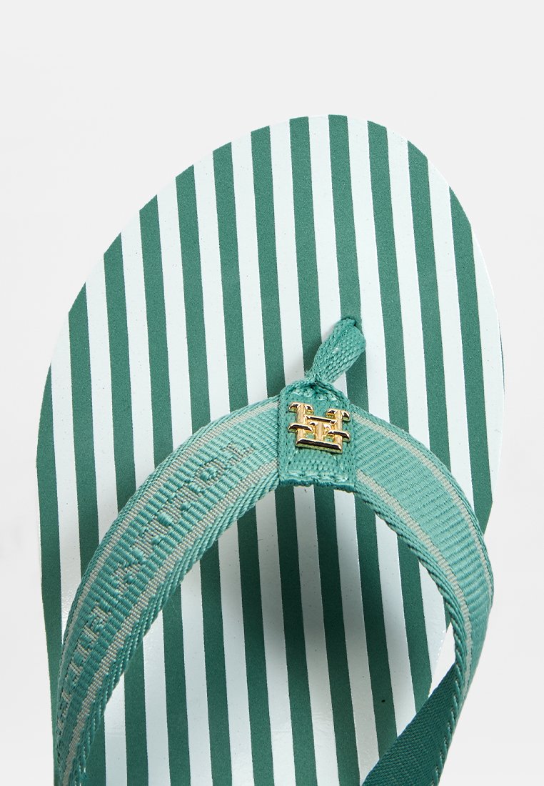 Tongs à rayures vertes avec un dessous texturé, des sangles en tissu et un accent de logo doré.