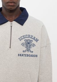 Svetlosivý mikiny s námorníckym golierom, predným zipsom a grafickou potlačou, ktorá zobrazuje dizajn chobotnice so textom "ICECREAM SKATEBOARDS".