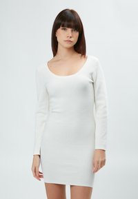 Hvid langærmet bodycon-kjole med rund halsudskæring. Den strukturerede stof har subtile mønstre og en tætsiddende silhuet, der når til midten af låret.