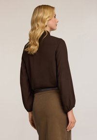 Blusa marrón de manga larga con mangas abullonadas, textura suave y escote redondo, combinada con una falda marrón a juego.