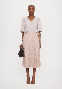 Short-sleeve, V-neck top in shiny light pink fabric paired with a mid-length, textured skirt featuring floral appliqués in a matching shade.