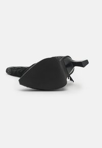 Zapato de tacón alto negro con puntera puntiaguda, parte superior de tela texturizada y tacón rectangular con suela de goma.