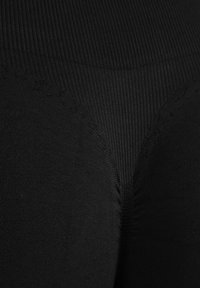 Gros plan sur un tissu noir texturé avec un motif côtelé et des détails de coutures courbes.