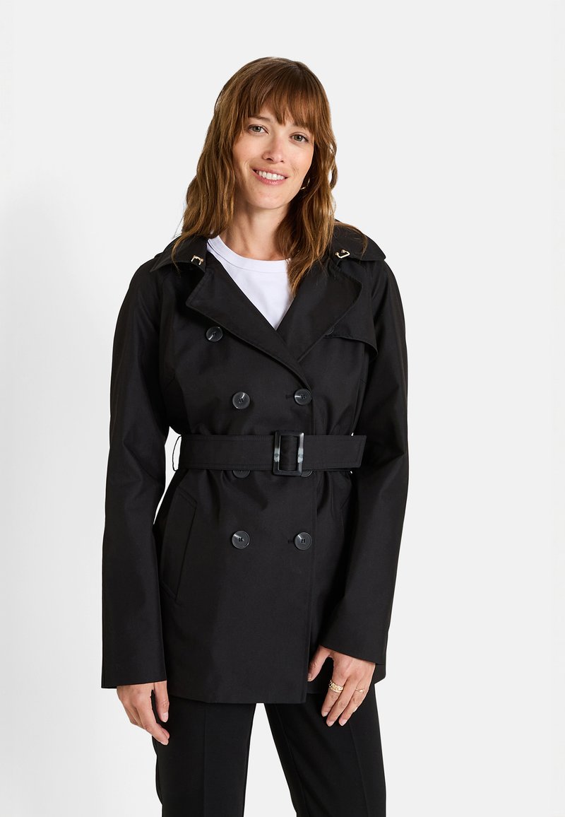 Manteau noir en trench avec un design à double boutonnage, taille ceinturée et grands boutons. Il présente un col et un tissu lisse et imperméable.