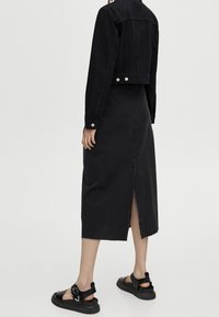 Černá džínsová bunda a sukně, která má zkrácený střih, rozparek vzadu a texturovanou tkaninu. Doplněno černými sandály.