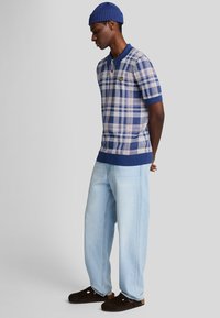 Polo a maniche corte a quadri nei colori blu, bianco e rosa, con colletto e orlo blu uniforme. Abbinato a jeans azzurri a taglio largo e zoccoli scuri.