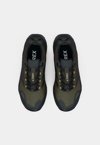 Scarpe da trekking verdi e grigie con tessuto testurizzato, suola in gomma e dettagli gialli. Presentano una chiusura con lacci e un logo del marchio ben visibile.