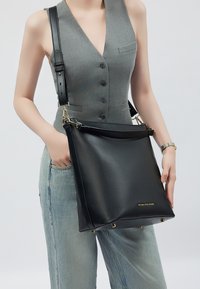 Borsa a spalla in pelle nera con tracolla removibile, design minimalista, con logo dorato e quattro piedi metallici per stabilità.