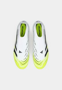 Baskets blanches de sport avec des rayures noires et des accents jaunes ; tige texturée avec un design sans lacets. Présente le logo "Predator" sur les semelles intérieures.
