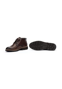 Botas de cuero marrón hasta el tobillo con punta redondeada, diseño de cordones, costuras en contraste y una suela de goma texturizada. Incluye patrones de relieve.