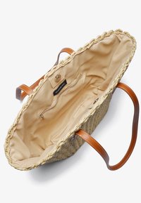 Sac fourre-tout en paille tissée avec poignées en cuir marron clair. Intérieur doublé en tissu beige, avec poche zippée et fermeture magnétique. Design à ouverture ouverte.