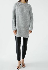 Pull en tricot à côtes gris avec un col rond et des manches longues, associé à des leggings en simili cuir noirs et des tongs noires.