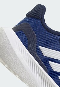 Blue athletic shoe with mesh upper, textured navy accents, and a white textured outsole. Features three white stripes on the side.