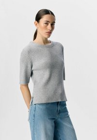 Maglione grigio a coste con maniche corte, scollatura rotonda, fessure laterali e texture morbida, abbinato a jeans blu a vestibilità rilassata.