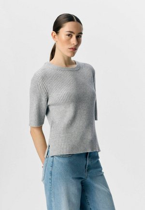 Grijs geribbeld sweater met korte mouwen, ronde halslijn, zijsplitten en een zachte textuur, gecombineerd met blauwe relaxed-fit jeans.