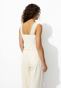 Camisole à bordure en dentelle en blanc cassé, avec un corsage ajusté et de larges bretelles ; accompagnée d'un pantalon taille haute de couleur beige clair.