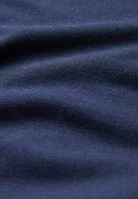 Dunkelblauer gestrickter Stoff mit sichtbarer Webstruktur und weichen Falten, die subtile Schatten und Lichtreflexe erzeugen.