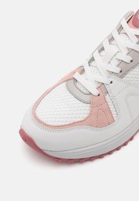 Avant de chaussure de sport blanc et rose avec tissu en mesh, surcouches en daim, lacets blancs et semelle en caoutchouc texturée, présenté sur un fond blanc.