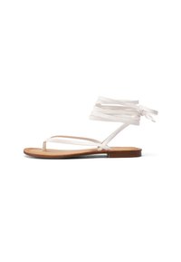 Sandali flat bianchi con sottili cinghie incrociate e un anello per le dita. La soletta è in pelle marrone, e la suola è minimalista con una leggera lucentezza.