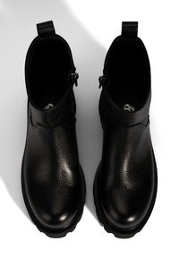Bottines en cuir noir avec une finition texturée, bout rond et fermeture éclair de chaque côté. Elles sont dotées d'un tirant pour un enfilage facile.