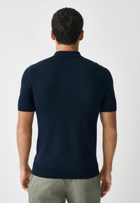 Tumesinine lühikeste varrukatega polo-särk soonikulise krae ja äärisega, valmistatud siledast, kergest kangast, iseloomustab kitsas lõige.