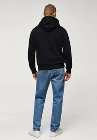 Sweat à capuche noir avec un col arrondi et une poche kangourou, associé à un jean en denim bleu clair et des baskets blanches. Design simple et décontracté.