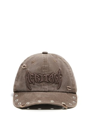 Casquette de baseball marron usée avec des œillets métalliques ronds sur la visière et le mot brodé en relief "HERITAGE" à l'avant.